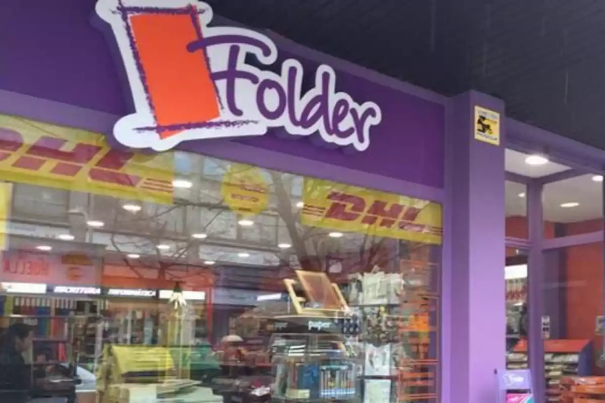 Fachada de una papelería con letrero morado y blanco que dice Folder y vitrinas mostrando material de oficina Fachada de una papelería con letrero morado y blanco que dice Folder y vitrinas mostrando material de oficina