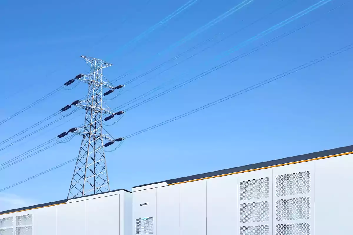 Torre de alta tensión y cables eléctricos sobre un edificio blanco bajo un cielo despejado