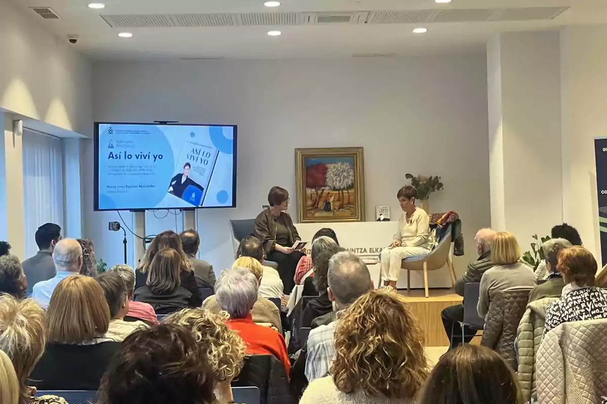 Presentación de un libro ante un público en una sala, con dos mujeres sentadas al frente y una pantalla mostrando la portada del libro "Así lo viví yo"