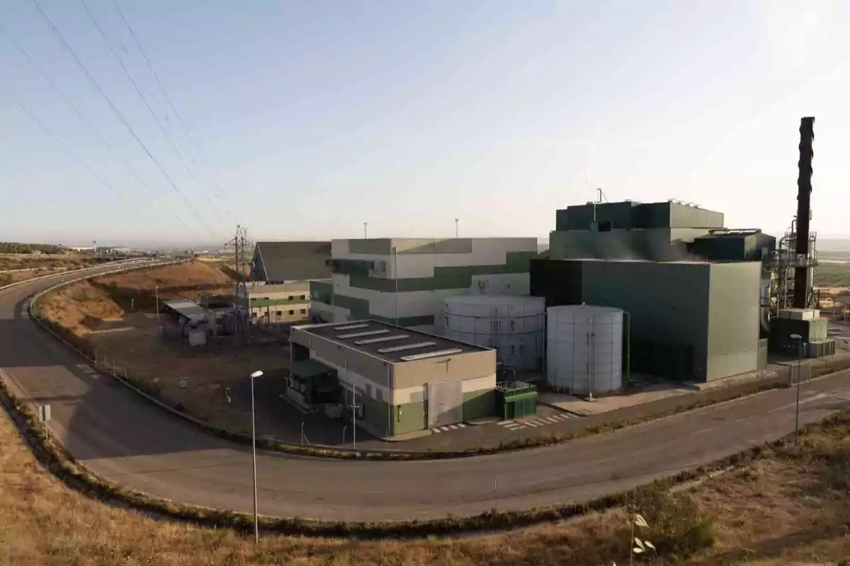 Vista de una planta industrial con varios tanques y edificios rodeados por una carretera y líneas eléctricas en un entorno rural