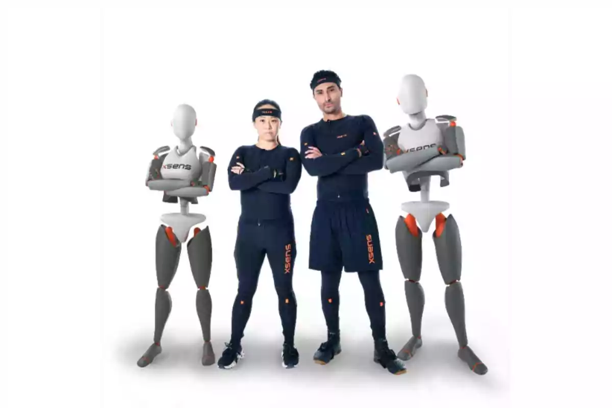 Dos personas con trajes de captura de movimiento posan con los brazos cruzados junto a dos maniquíes grises que también tienen los brazos cruzados