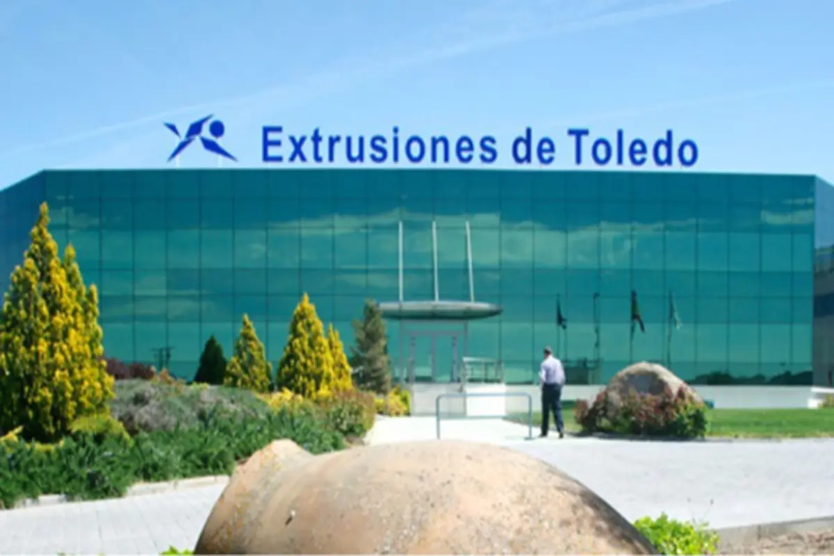 Fachada acristalada de la empresa Extrusiones de Toledo con jardines y una persona caminando hacia la entrada