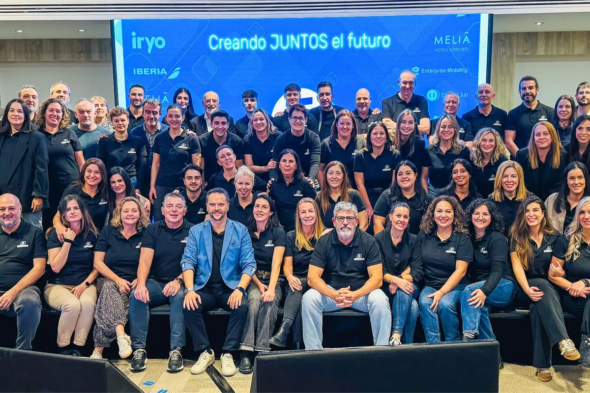 Grupo numeroso de personas posando sonrientes en un auditorio, la mayoría lleva camisetas negras y al fondo hay una pantalla azul con el texto Creando JUNTOS el futuro