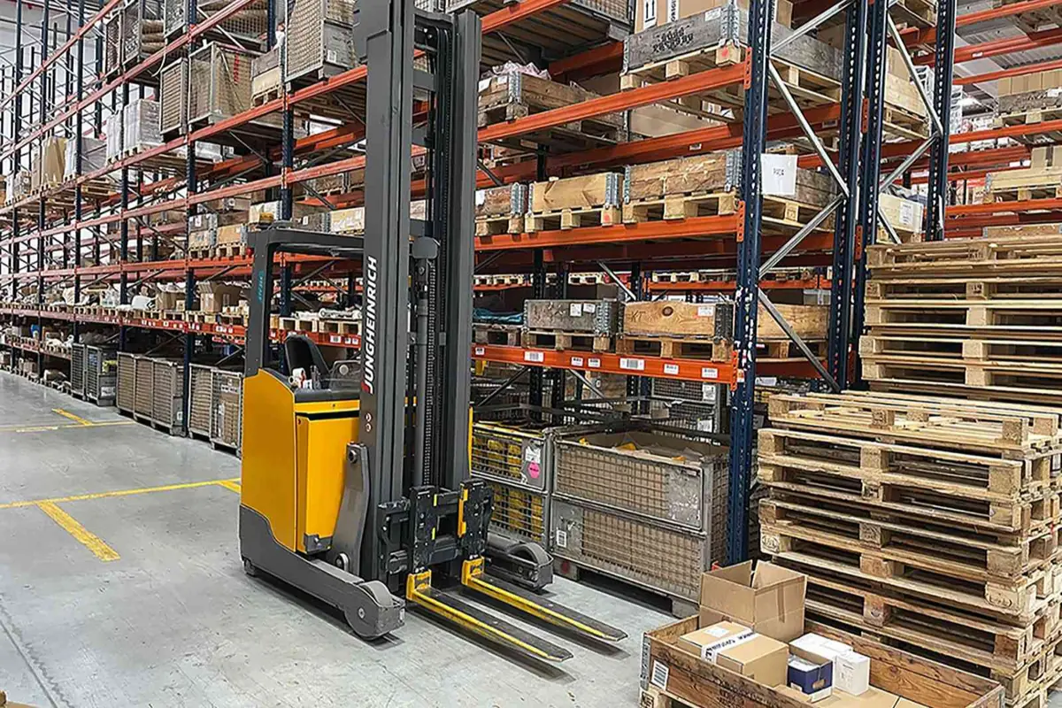 Carretilla elevadora amarilla en un almacén con estanterías altas llenas de palés y cajas de mercancía Carretilla elevadora amarilla en un almacén con estanterías altas llenas de palés y cajas de mercancía