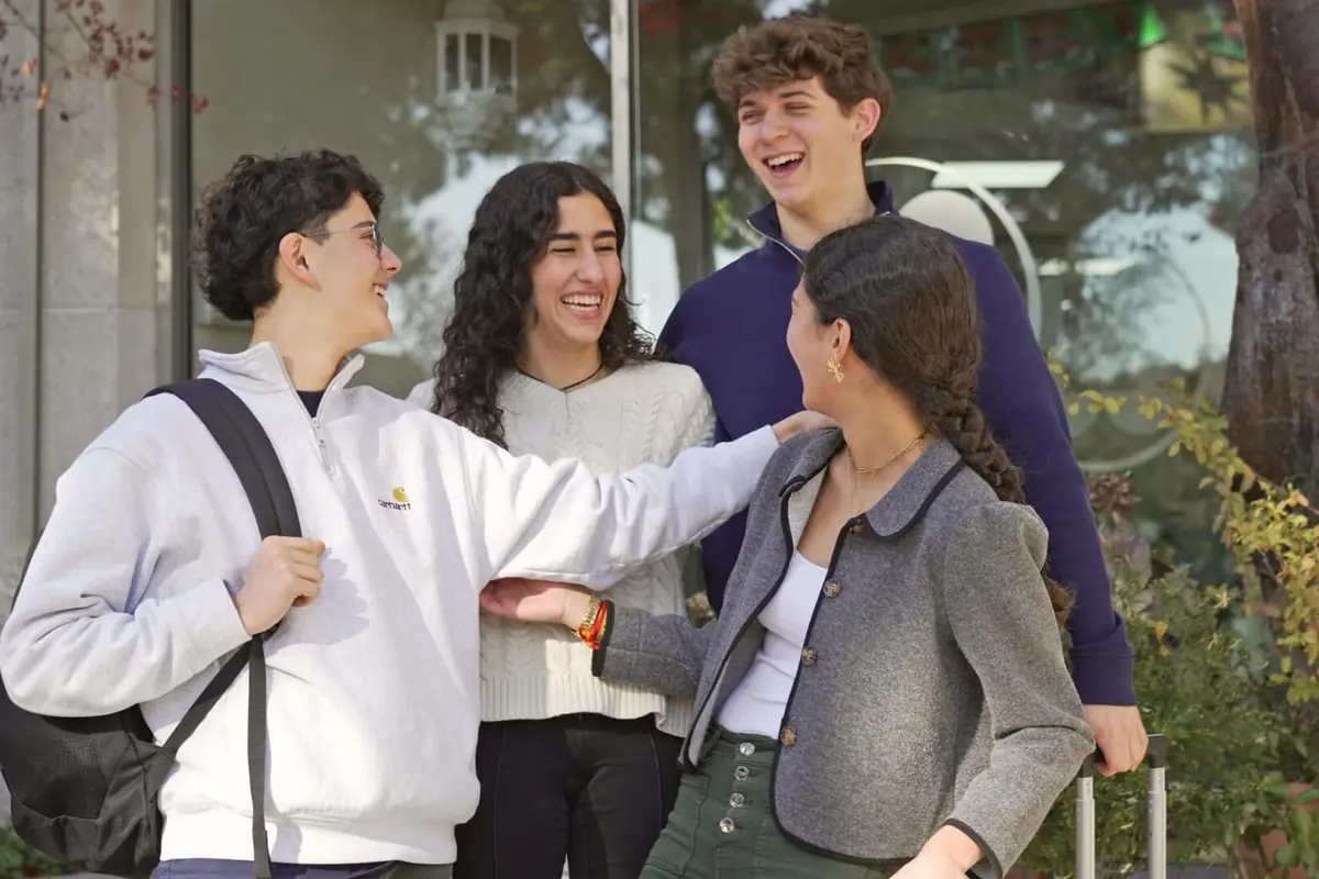 Cuatro jóvenes conversan y ríen juntos al aire libre frente a un edificio rodeado de plantas