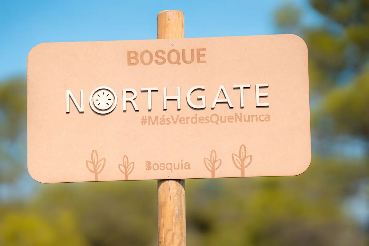 Letrero de madera con el texto Bosque Northgate y el hashtag MásVerdesQueNunca sobre un fondo de árboles y cielo azul