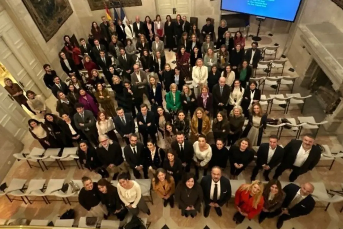 Un grupo numeroso de personas vestidas de manera formal posando para una foto en el interior de un elegante salón con sillas y una pantalla al fondo