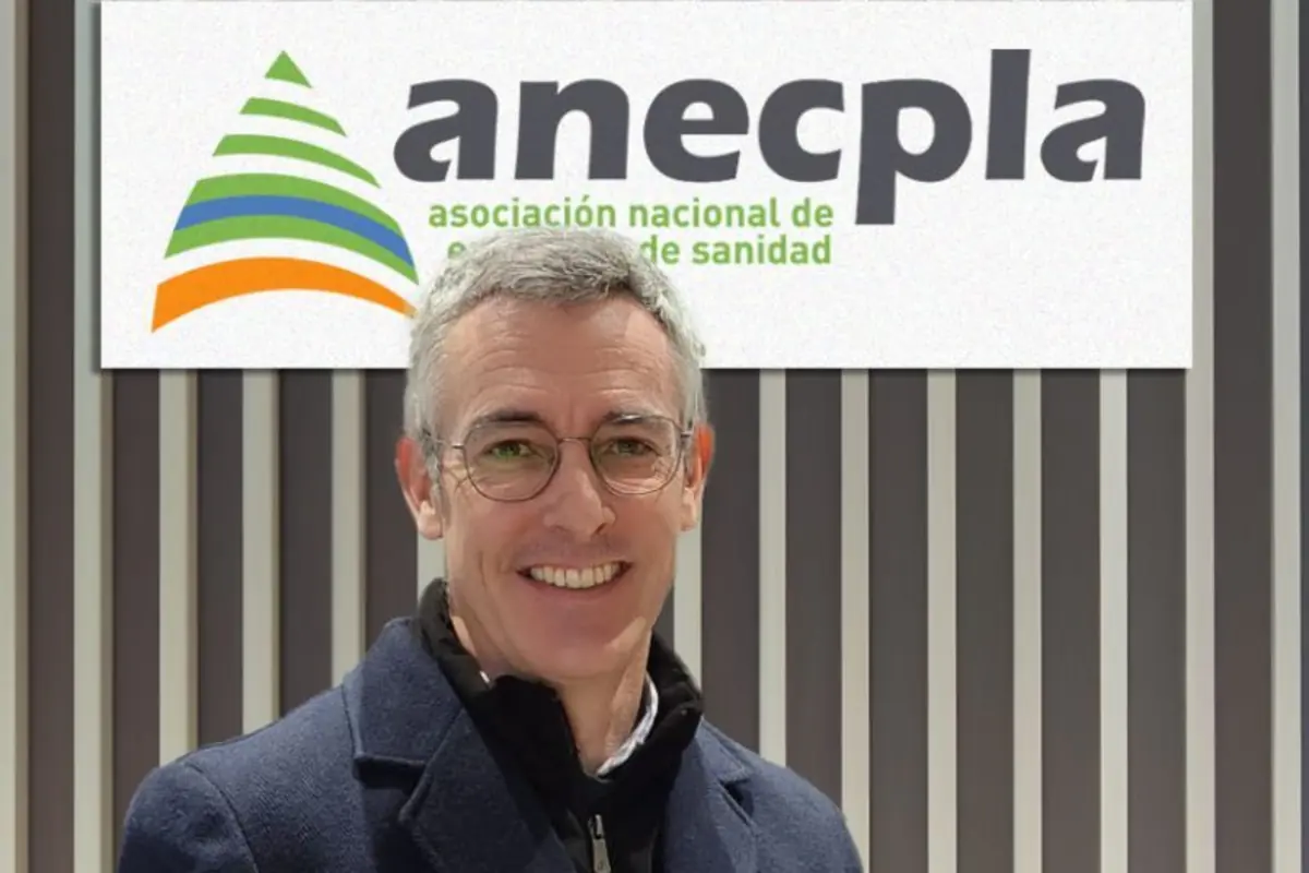 Hombre con gafas sonriendo frente a un cartel de la asociación nacional de empresas de sanidad anecpla