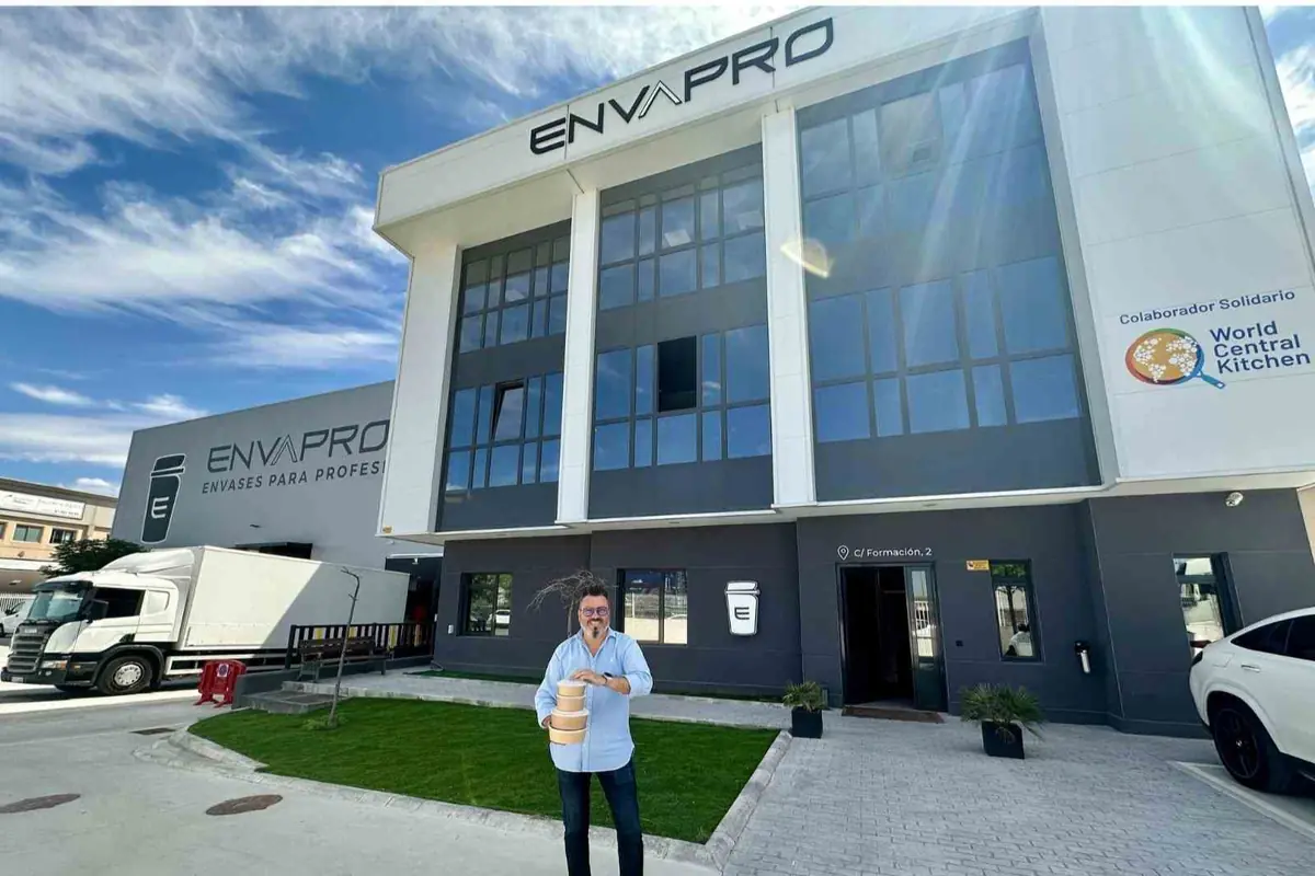 Hombre sosteniendo varios envases frente a la fachada de la empresa ENVAPRO con camión de reparto y logotipo de World Central Kitchen en el edificio