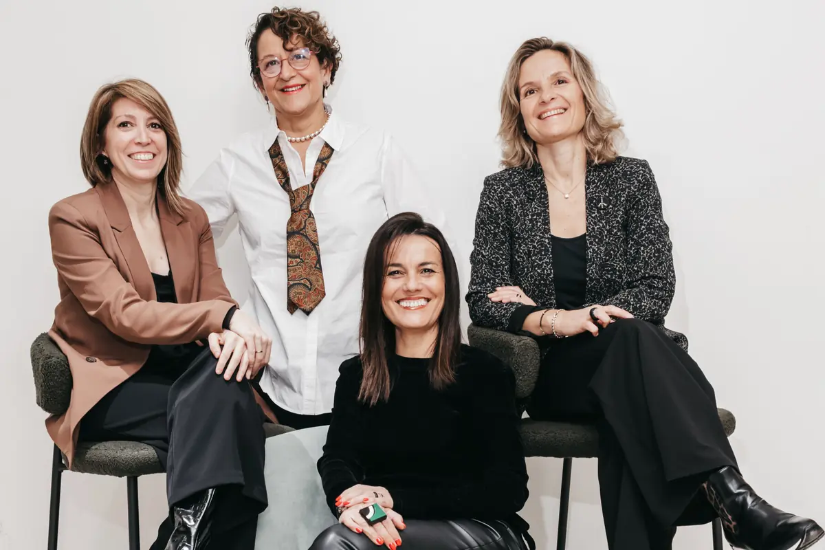 Cuatro mujeres adultas posan sonrientes en un entorno profesional sentadas en sillas frente a un fondo blanco