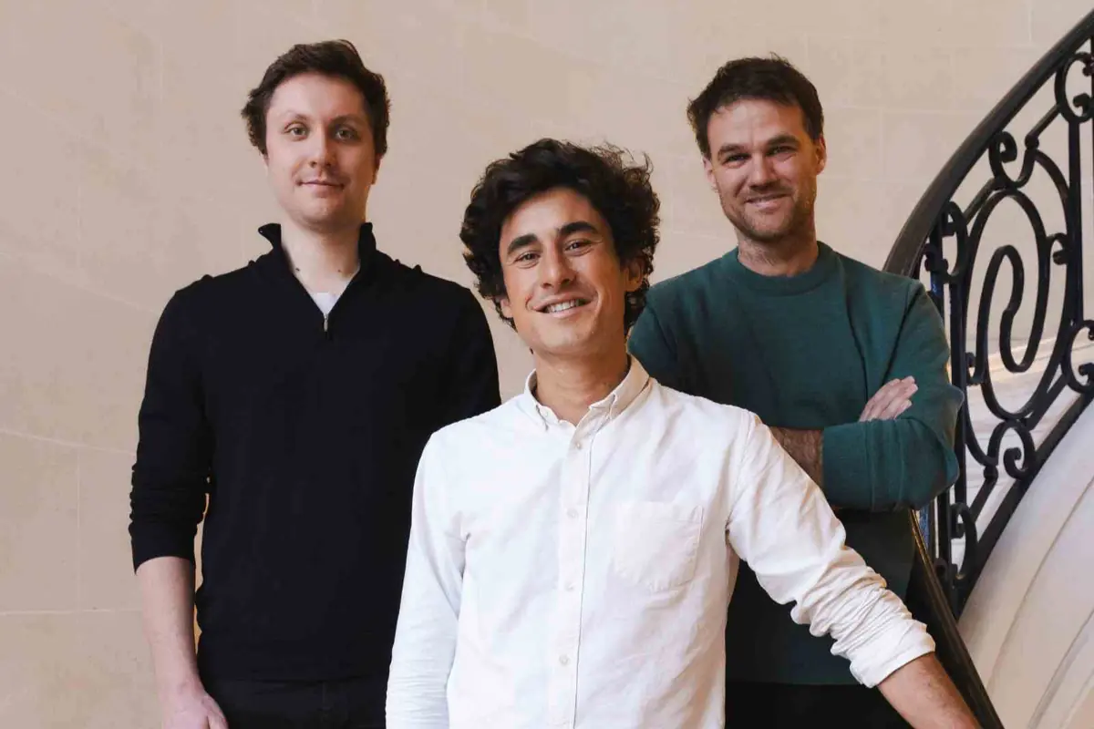 Tres hombres jóvenes posan sonrientes en el interior de un edificio junto a una barandilla elegante Tres hombres jóvenes posan sonrientes en el interior de un edificio junto a una barandilla elegante