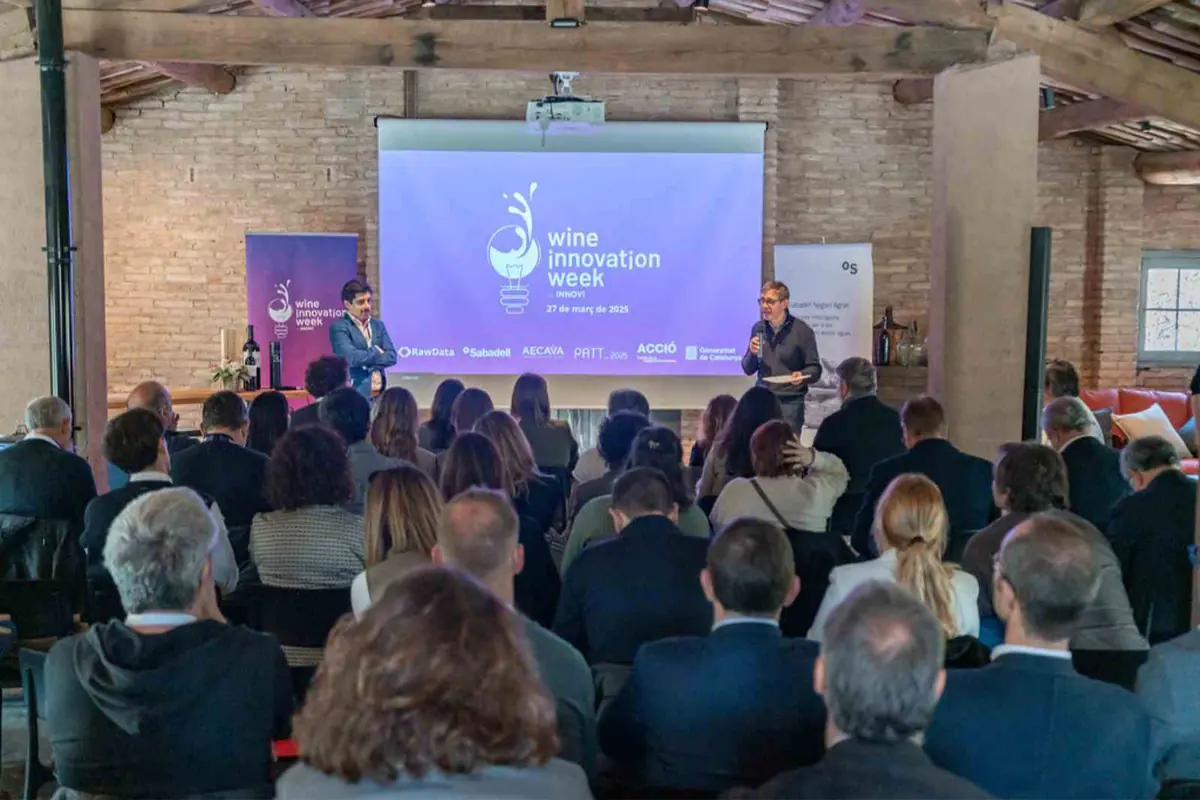 Conferencia sobre innovación en el sector del vino con dos ponentes frente a una pantalla grande y un público sentado en una sala de estilo rústico