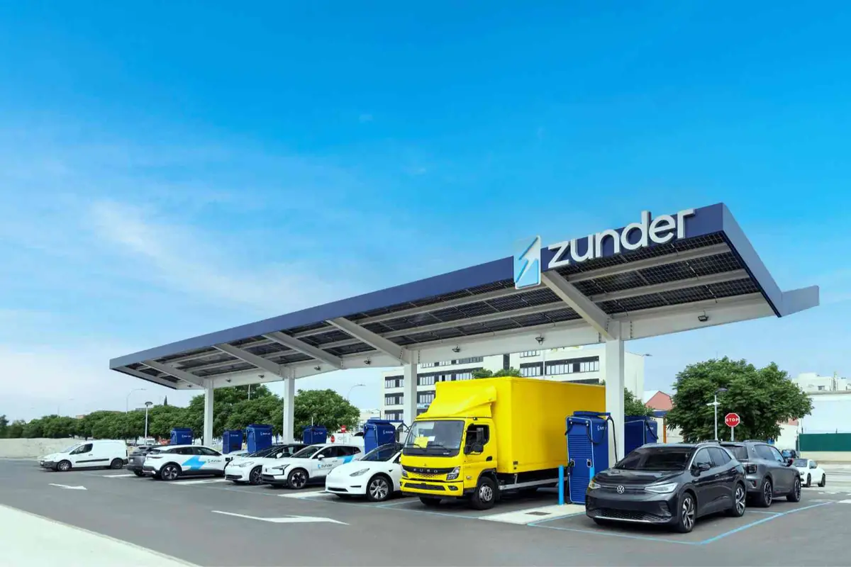 Estación de carga Zunder con varios vehículos eléctricos y una furgoneta amarilla recargando bajo una gran marquesina en un día despejado Estación de carga Zunder con varios vehículos eléctricos y una furgoneta amarilla recargando bajo una gran marquesina en un día despejado