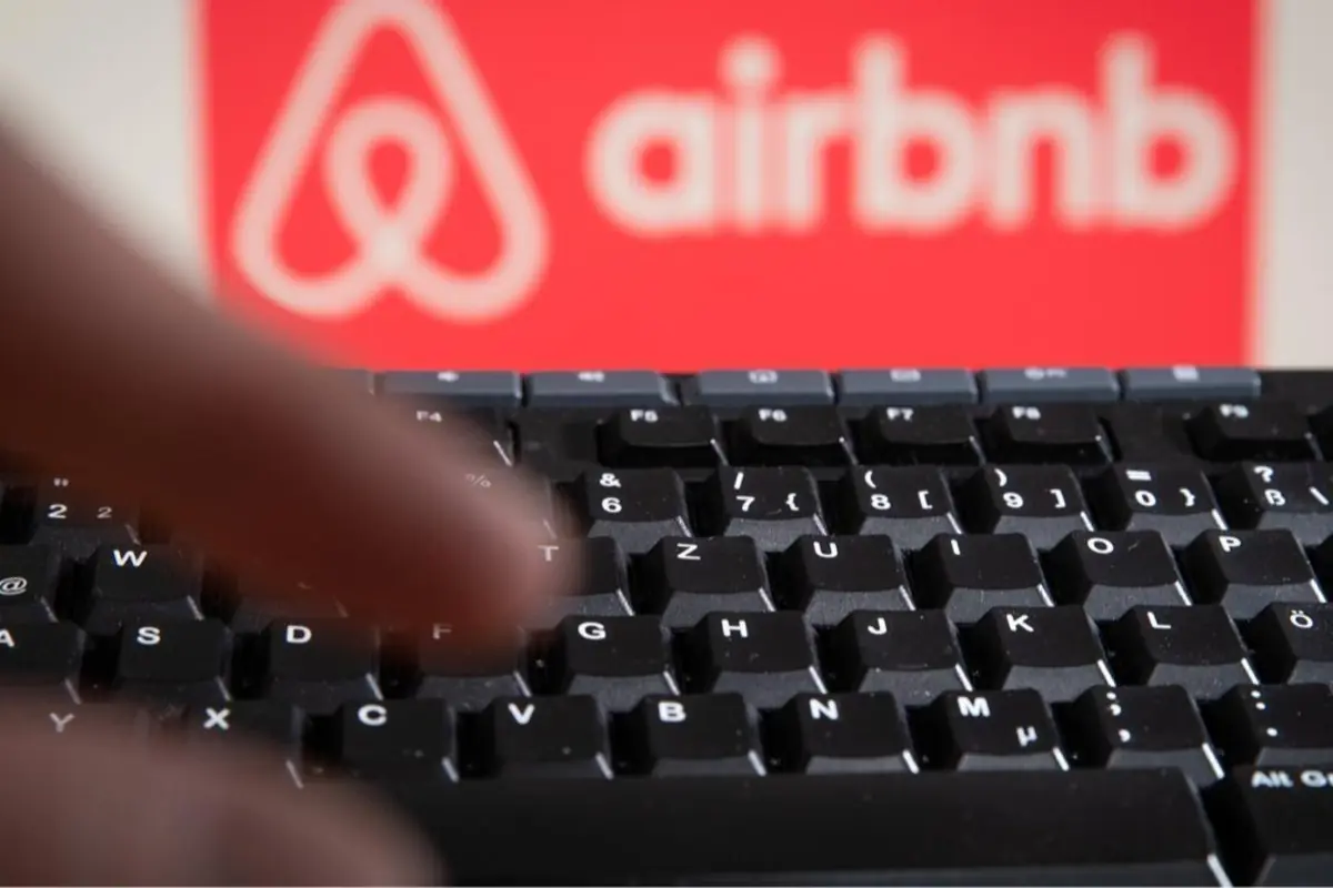 Manos escribiendo en un teclado de computadora con el logo de Airbnb desenfocado al fondo Manos escribiendo en un teclado de computadora con el logo de Airbnb desenfocado al fondo