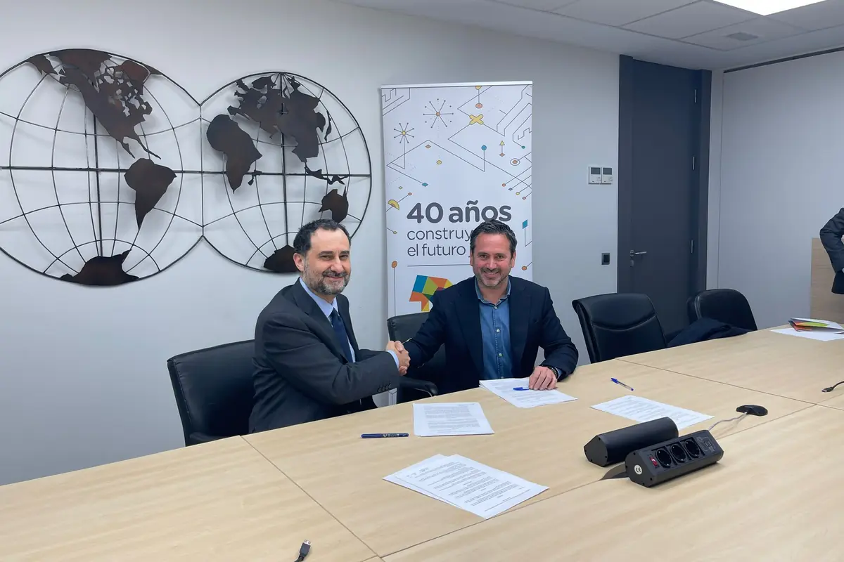 Dos hombres de negocios se dan la mano en una sala de reuniones frente a documentos firmados con un mapa del mundo metálico en la pared y un cartel que dice 40 años construyendo el futuro