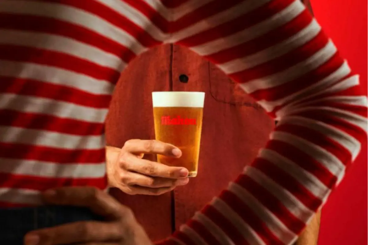 Persona con camisa roja sosteniendo un vaso de cerveza visto a través de los brazos de otra persona con camiseta de rayas rojas y blancas