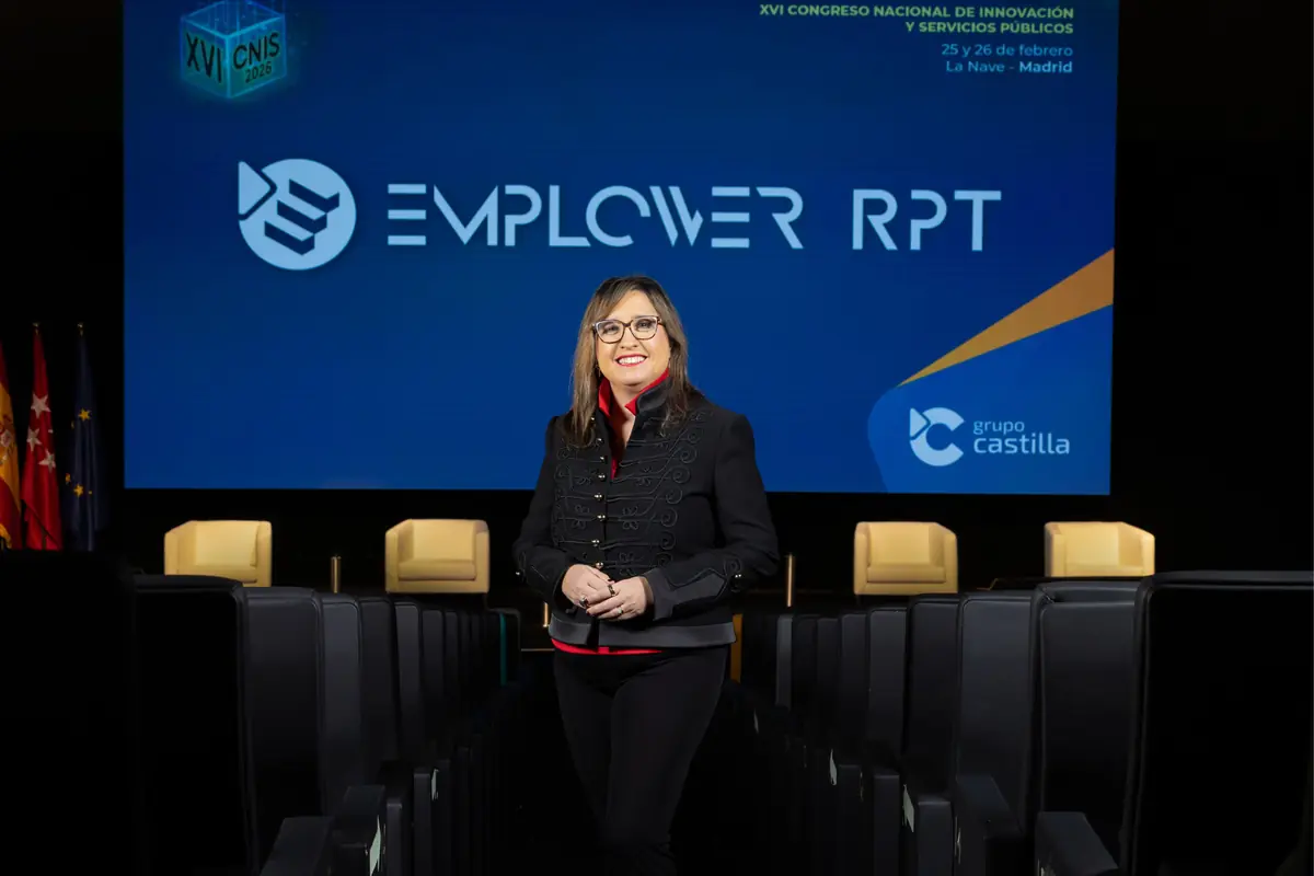 Mujer sonriente de pie en el pasillo de un auditorio vacío con un gran escenario al fondo donde se proyecta el logotipo de Empower RPT y la información del XVI Congreso Nacional de Innovación y Servicios Públicos en Madrid