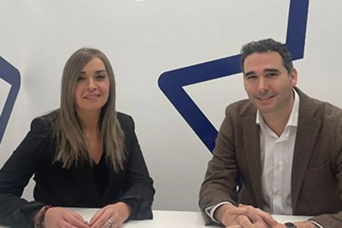 Dos personas sentadas a una mesa sonriendo en un entorno de oficina con un diseño geométrico azul en la pared de fondo