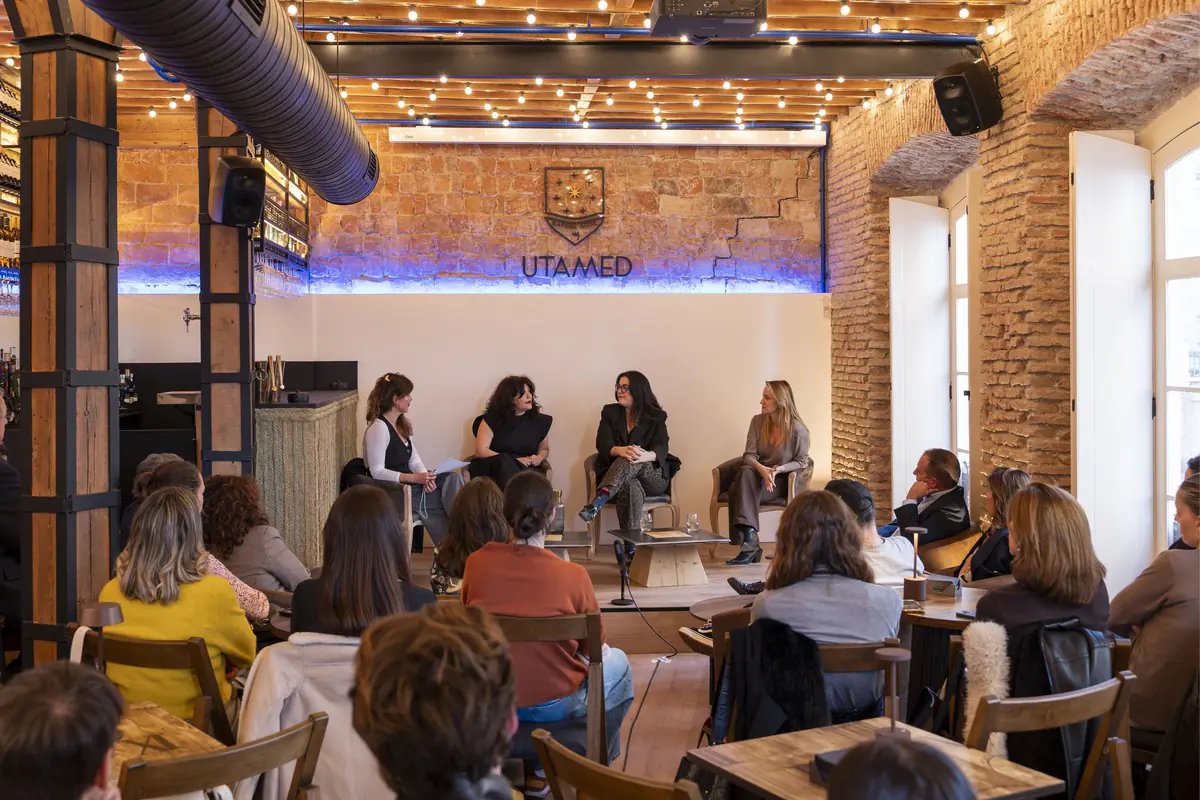 Mesa redonda con cuatro mujeres conversando frente a un público en un local acogedor de ladrillo visto y luces colgantes