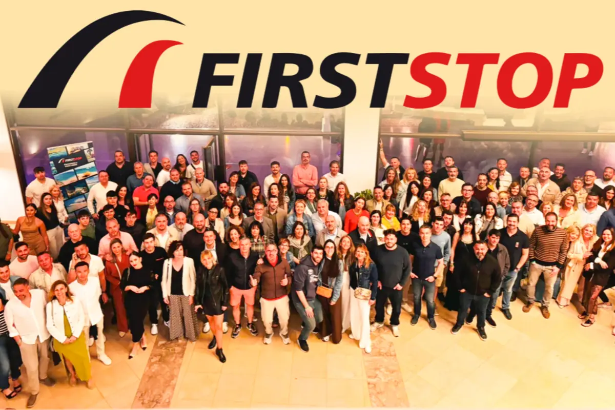 Gran foto de grupo de empleados de First Stop posando sonrientes bajo el gran logotipo de la empresa