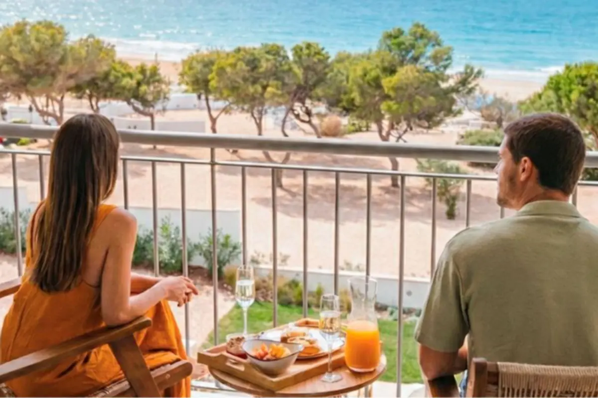 Pareja sentada en la terraza de un hotel desayunando mientras contempla la playa y el mar al fondo