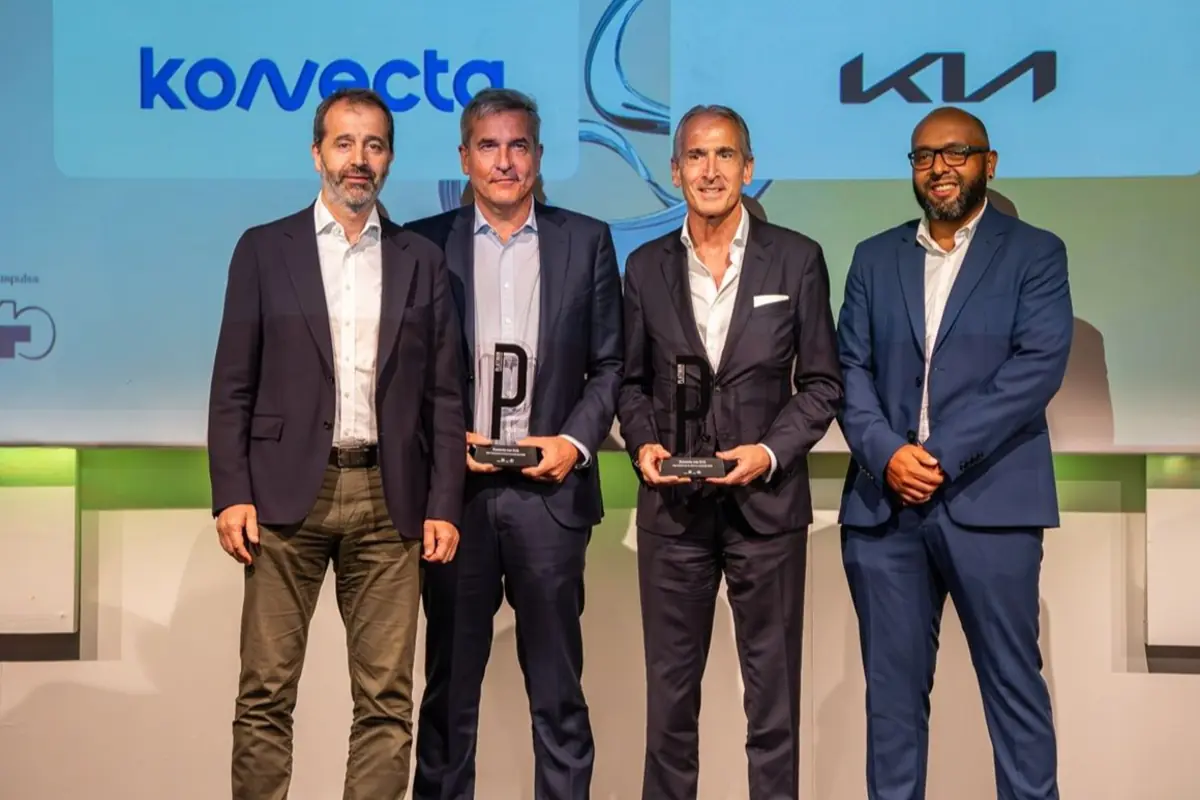 Cuatro hombres con traje posan en un escenario de entrega de premios dos de ellos sostienen trofeos negros con forma de letra P frente a una pantalla con logotipos de empresas