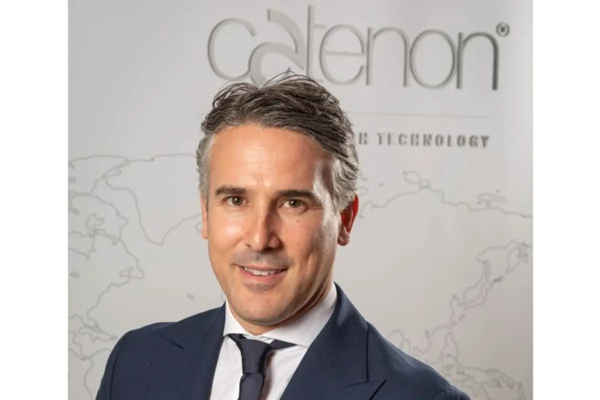 Retrato de un hombre de mediana edad con traje azul marino y corbata oscura sonriendo frente a un fondo claro con el logotipo de Catenon y un mapa mundial estilizado