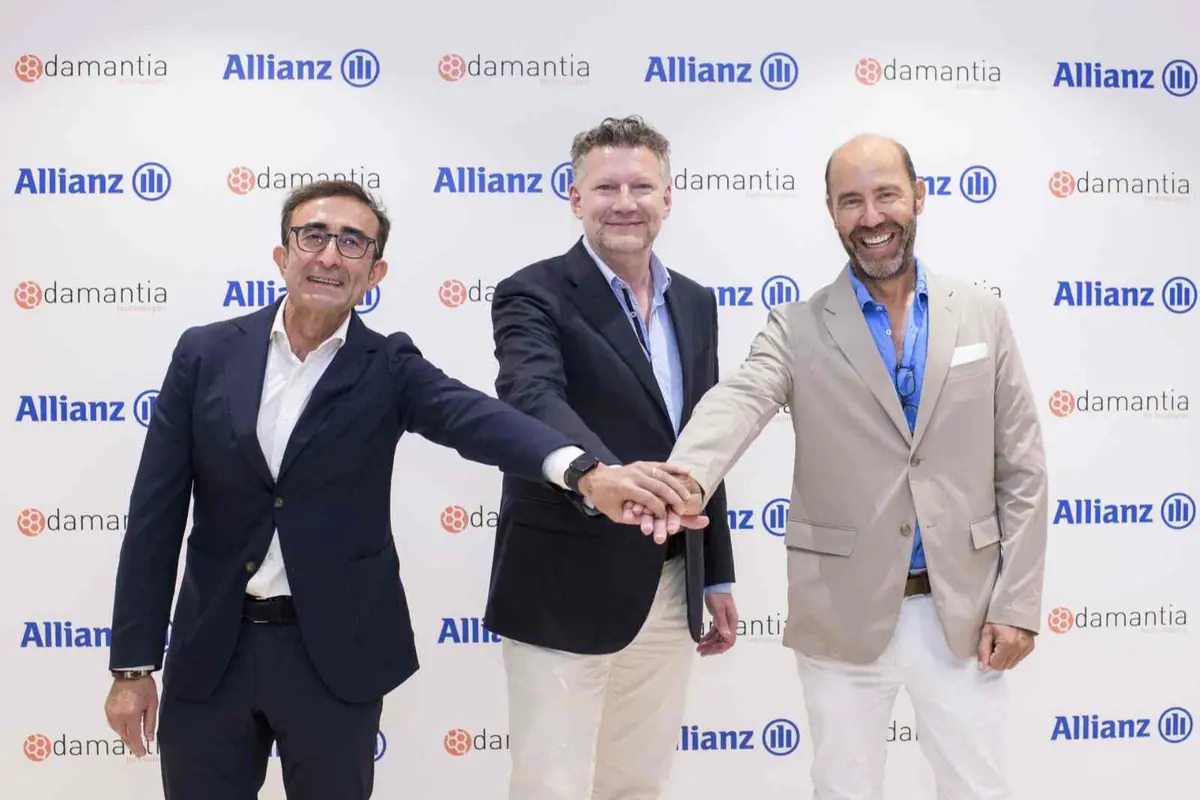 Tres hombres de negocios sonrientes posan dándose la mano frente a un fondo con los logotipos de Allianz y Damantia