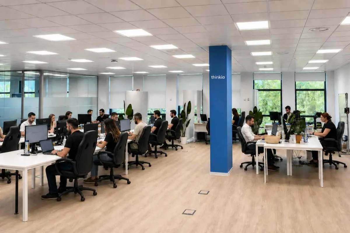 Oficina moderna de planta abierta con varias personas trabajando en escritorios con ordenadores y plantas decorativas