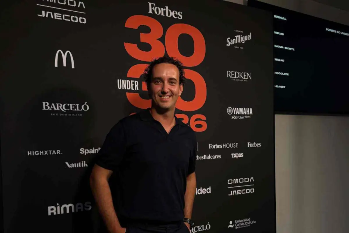 Hombre sonriendo frente a un photocall negro del evento Forbes 30 Under 30 rodeado de logotipos de marcas patrocinadoras