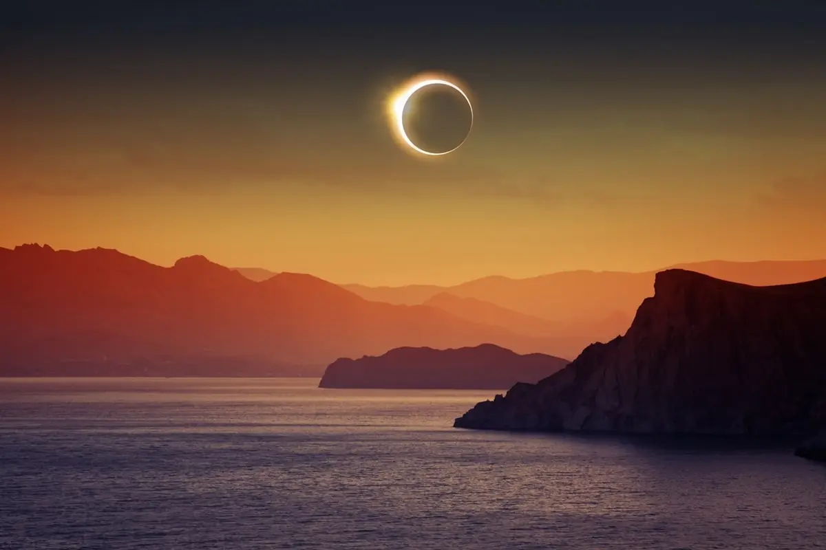 Eclipse solar anular sobre un paisaje costero con montañas al atardecer Eclipse solar anular sobre un paisaje costero con montañas al atardecer