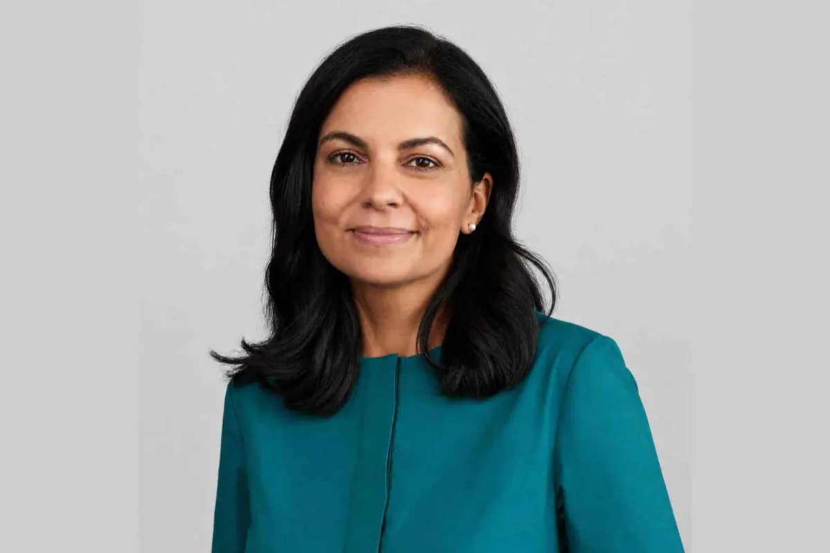 Retrato de una mujer de mediana edad con cabello oscuro y lacio, sonriendo levemente y vistiendo una blusa verde azulado sobre fondo gris claro