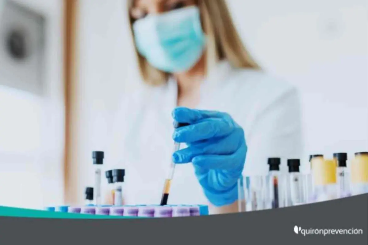 Profesional de laboratorio con mascarilla y guantes azules manipulando una muestra de sangre en tubos de ensayo