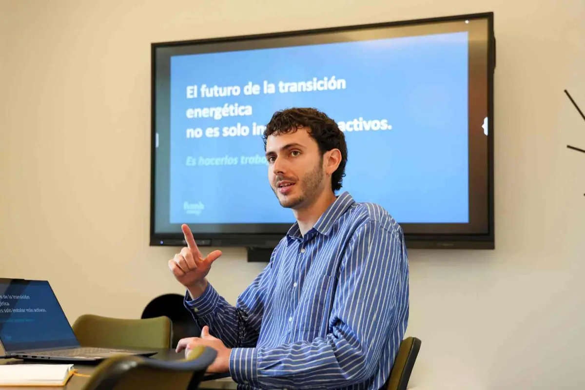 Hombre joven dando una presentación sobre transición energética frente a una pantalla con diapositiva azul en una sala de reuniones