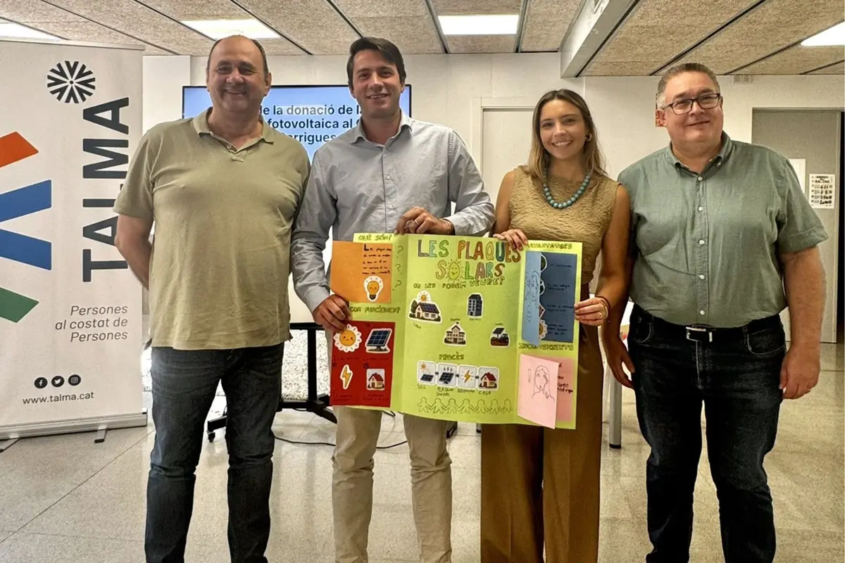 Cuatro personas posan en un interior junto a un cartel de la entidad Talma mientras dos de ellas sostienen un póster colorido sobre placas solares y energía fotovoltaica