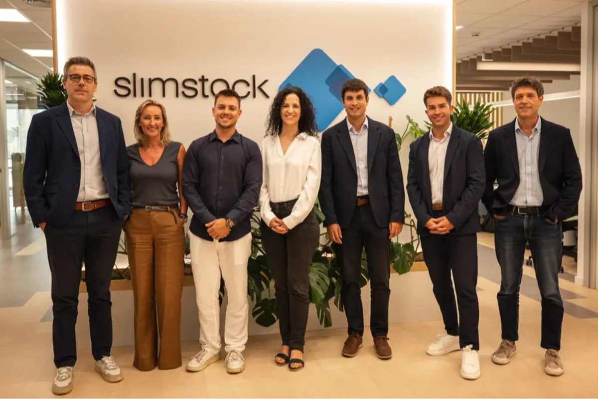 Equipo de siete personas posando de pie en una oficina moderna frente a un rótulo de Slimstock