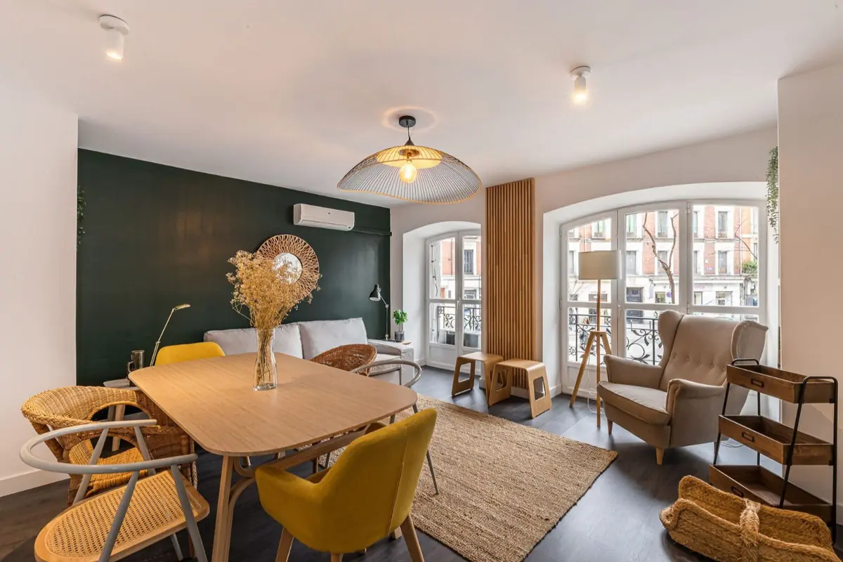 Salón comedor moderno y luminoso con mesa de madera y sillas amarillas y de mimbre sofá claro frente a pared verde oscuro sillón junto a grandes ventanales y decoración de estilo nórdico Salón comedor moderno y luminoso con mesa de madera y sillas amarillas y de mimbre sofá claro frente a pared verde oscuro sillón junto a grandes ventanales y decoración de estilo nórdico