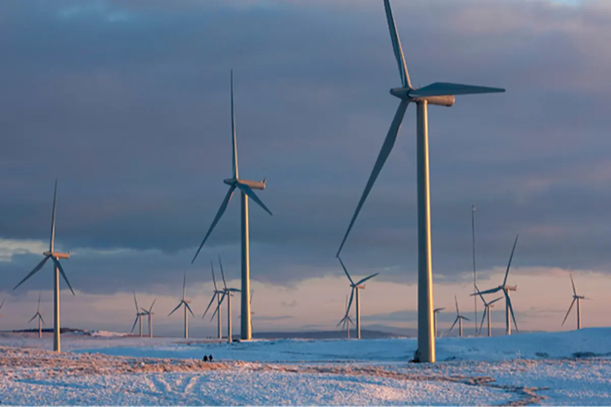Parque eólico con numerosos aerogeneradores sobre un paisaje nevado al atardecer