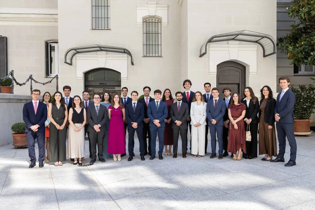 Grupo de jóvenes profesionales elegantemente vestidos posando en fila frente a la fachada de un edificio institucional