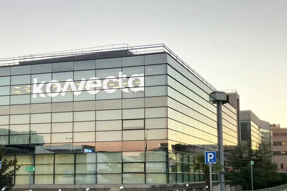 Edificio moderno de oficinas con fachada de vidrio reflejando el atardecer y el logotipo blanco de konecta en el lateral
