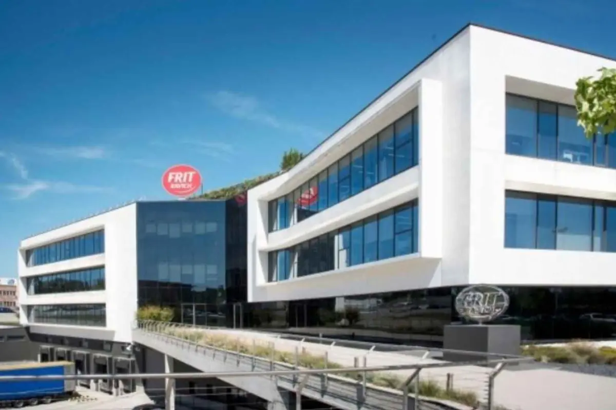 Edificio de oficinas moderno de la empresa FRIT con grandes ventanales de vidrio y pasarela exterior bajo un cielo despejado