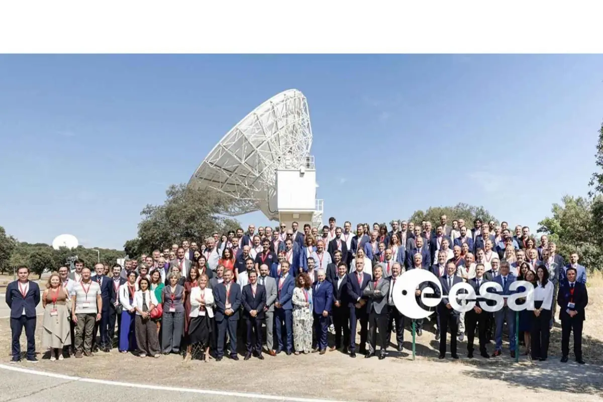 Grupo numeroso de personas posando frente a una gran antena parabólica al aire libre con el logotipo de la ESA en primer plano