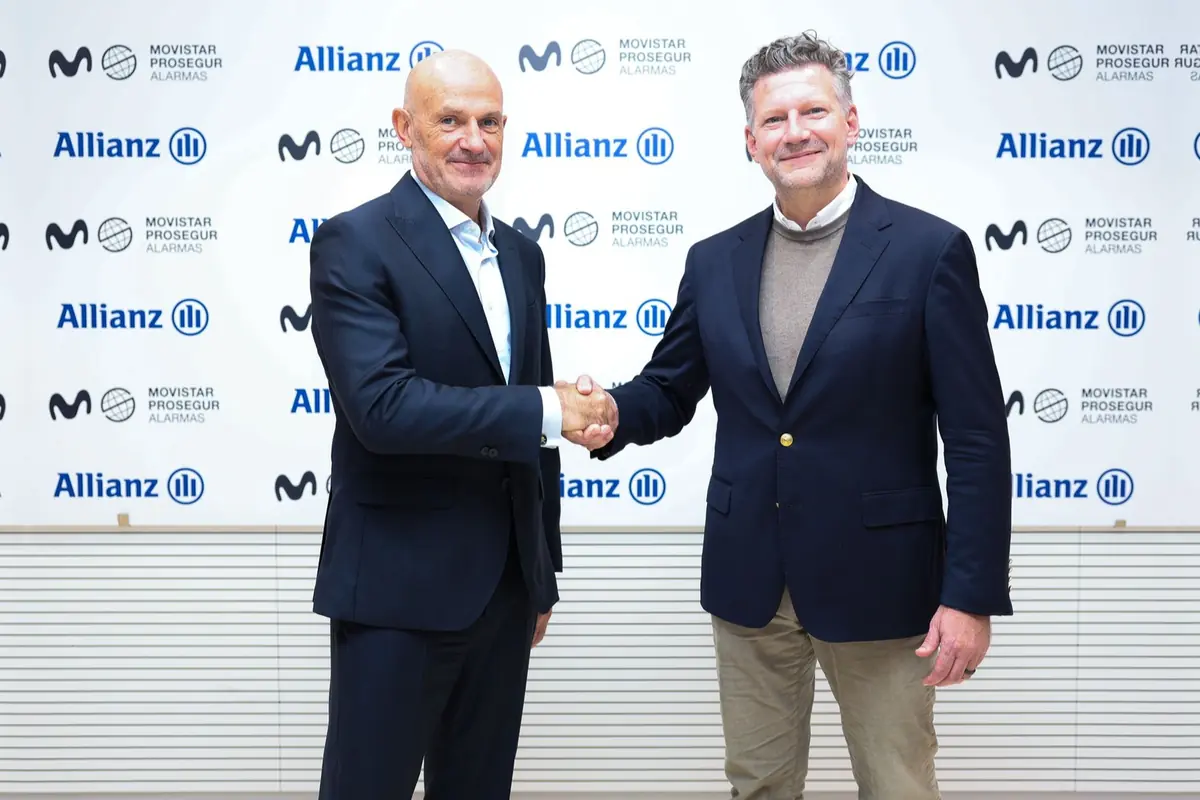 Dos ejecutivos con traje se dan la mano sonrientes frente a un fondo con los logotipos de Allianz y Movistar Prosegur Alarmas