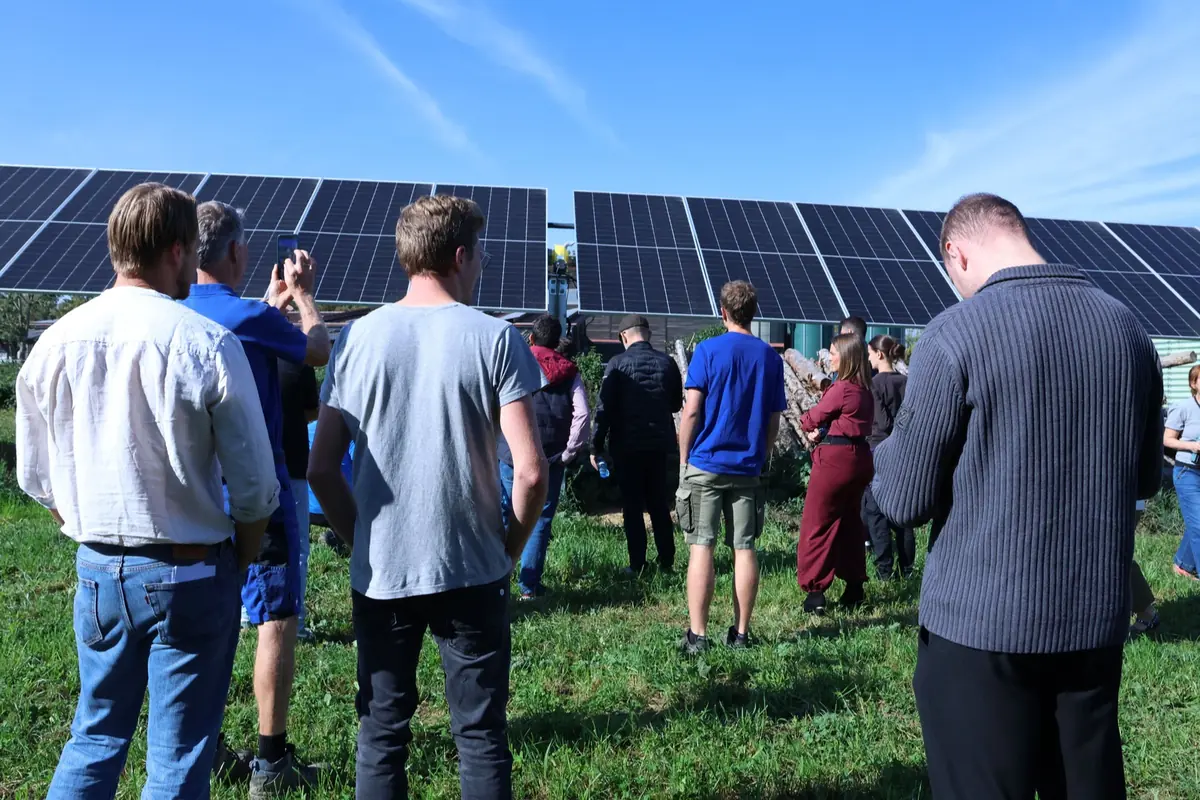 Grupo de personas reunidas al aire libre frente a grandes paneles solares en un día soleado