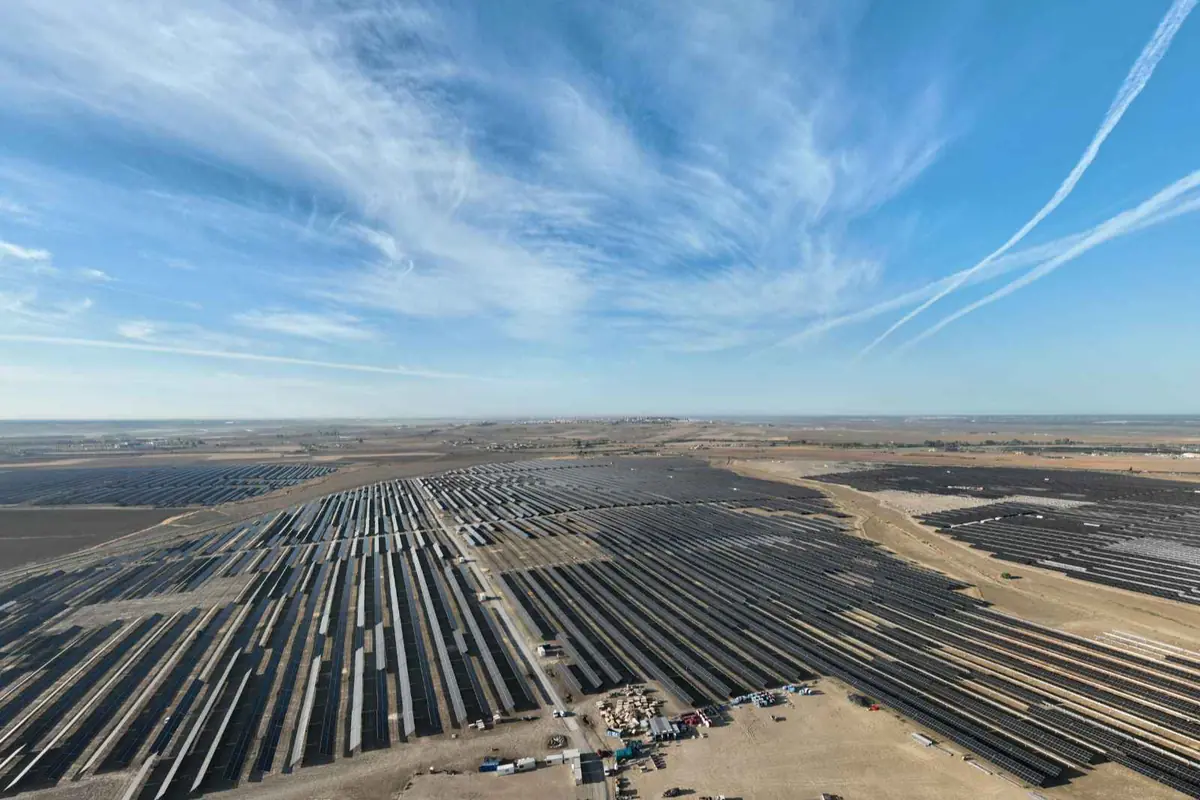 Vista aérea de una enorme planta solar fotovoltaica en un terreno árido bajo un cielo despejado con nubes delgadas y estelas de aviones Vista aérea de una enorme planta solar fotovoltaica en un terreno árido bajo un cielo despejado con nubes delgadas y estelas de aviones