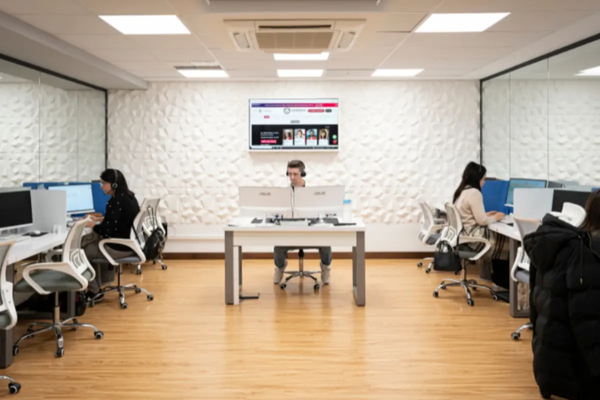 Oficina moderna con varias personas trabajando en ordenadores frente a escritorios blancos y paredes con paneles decorativos