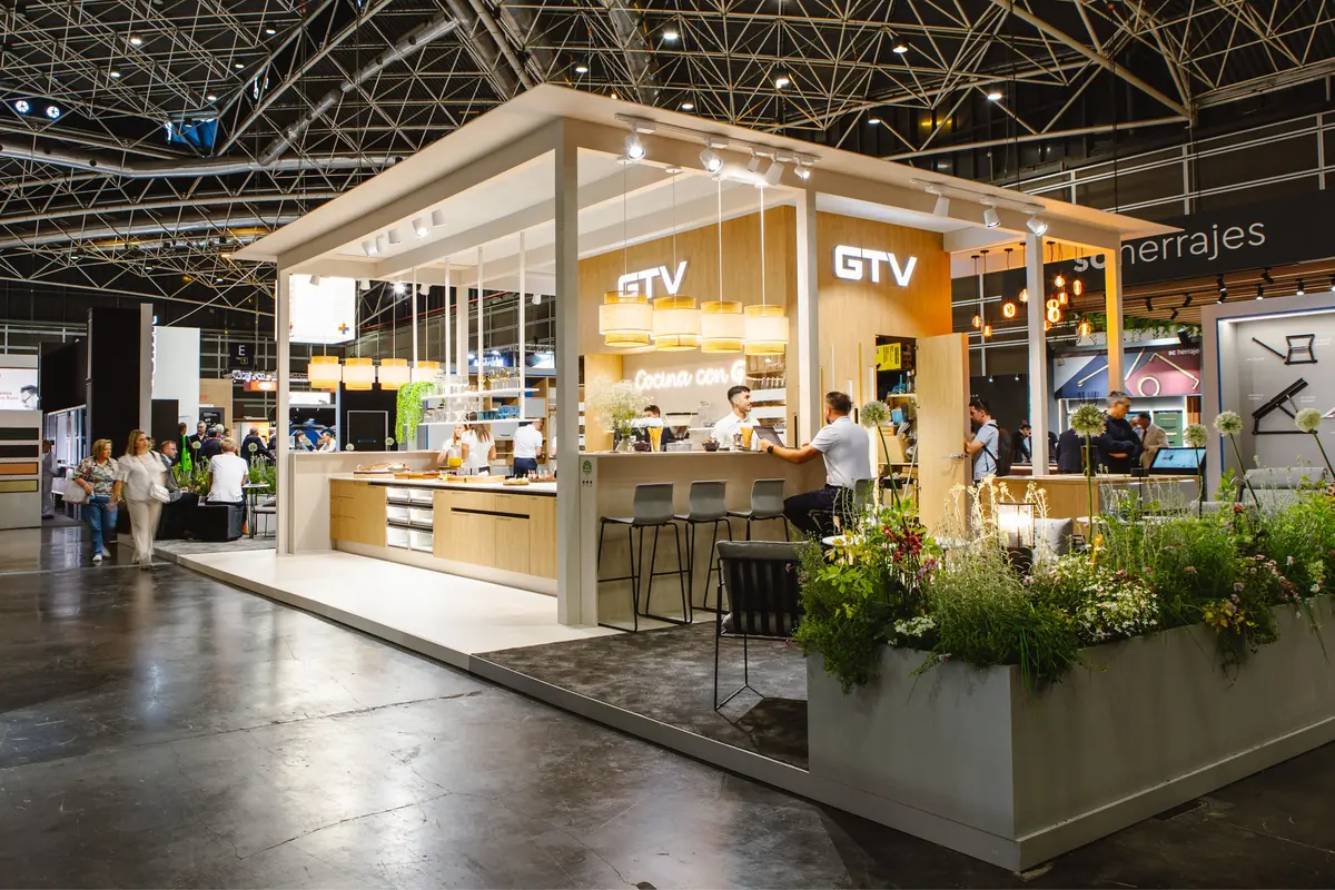 Stand moderno de cocina de la marca GTV en una feria comercial con barra, iluminación cálida, personas conversando y maceteros con plantas alrededor Stand moderno de cocina de la marca GTV en una feria comercial con barra, iluminación cálida, personas conversando y maceteros con plantas alrededor