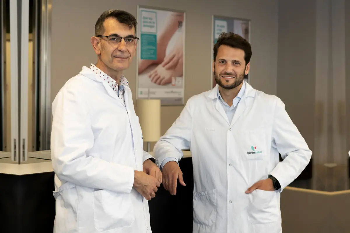 Dos profesionales sanitarios con bata blanca posan sonrientes en el interior de una clínica u hospital