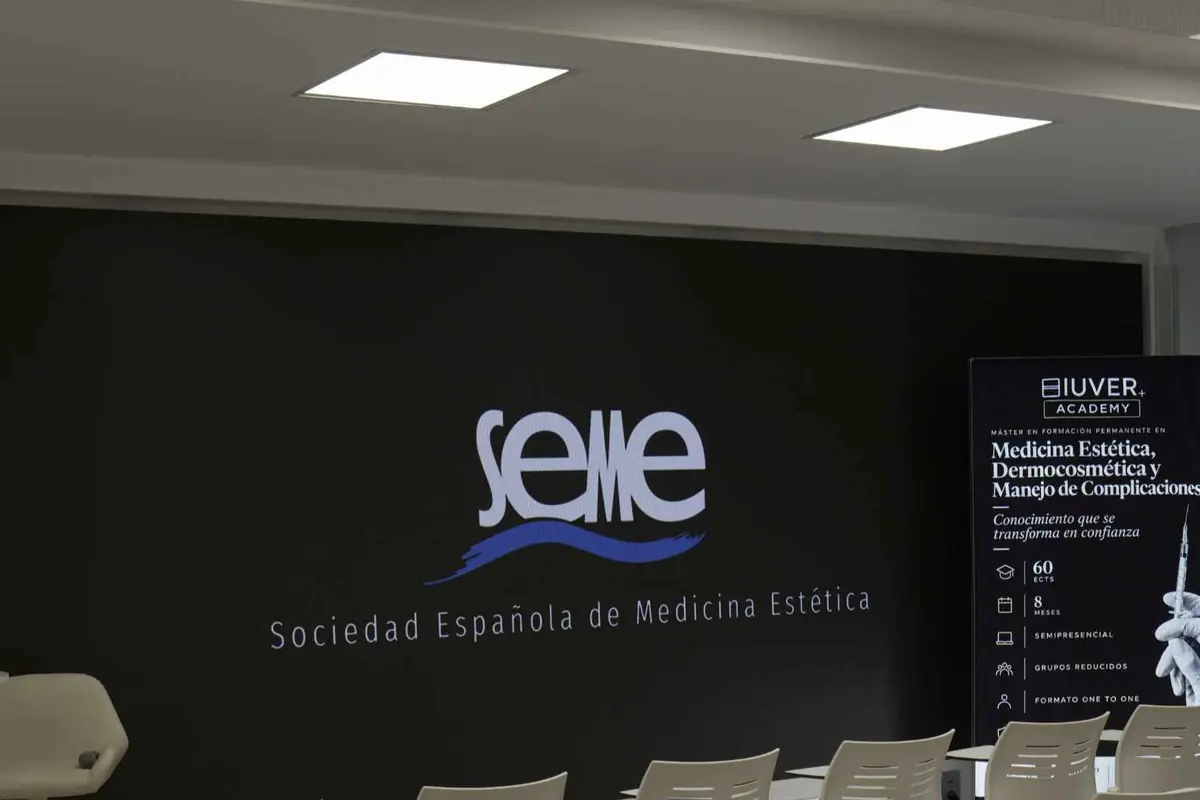 Sala de conferencias de la Sociedad Española de Medicina Estética con logo de SEME en pared negra y cartel informativo de un máster en medicina estética a la derecha