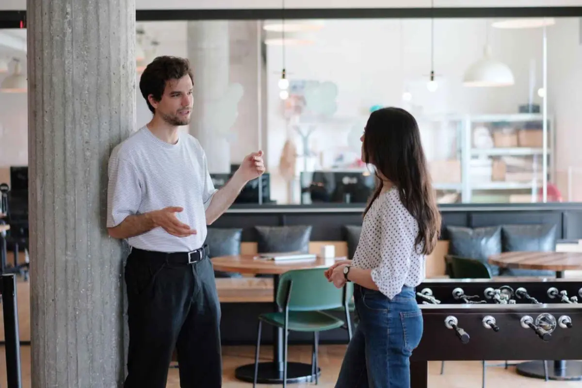Dos personas conversan de pie en una oficina moderna junto a una mesa de futbolín
